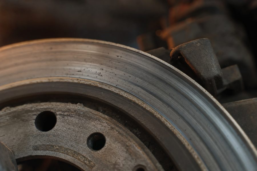 Eine gebrauchte Bremsscheibe mit abgenutzter Bremsspur, dahinter unscharf der Bremssattel